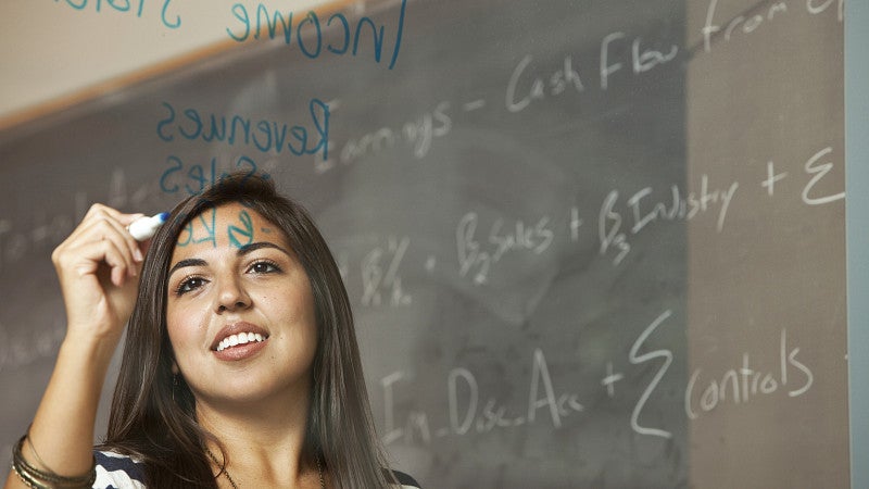 One student with a chalkboard in the background writing on glass with a whiteboard marker